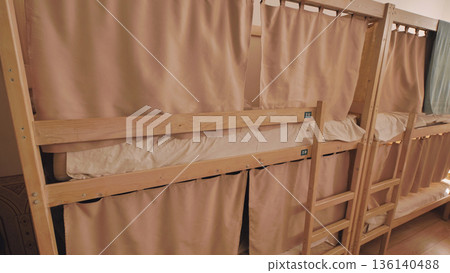 Hostel dormitory with wooden bunk beds, curtains providing privacy for travelers 136140488