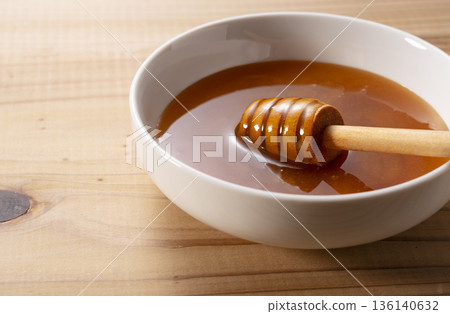 Honey dipper dipped in manuka honey in a white bowl (close-up, wood grain background) Honey dipper dipped in manuka honey in a white bowl (close-up, wood grain background) 136140632