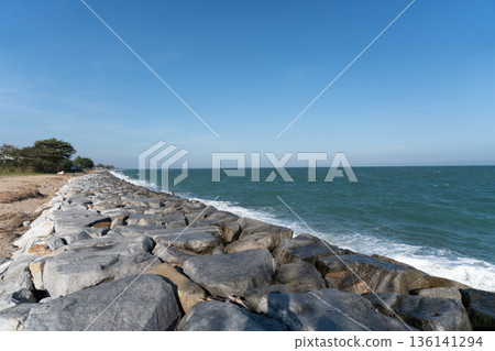 Peaceful landscape view with strong rock barrier protecting coast against blue sea wave under clear sky on bright sunny summer day Peaceful landscape view with strong rock barrier protecting coast against blue sea wave under clear sky on bright sunny summer day 136141294