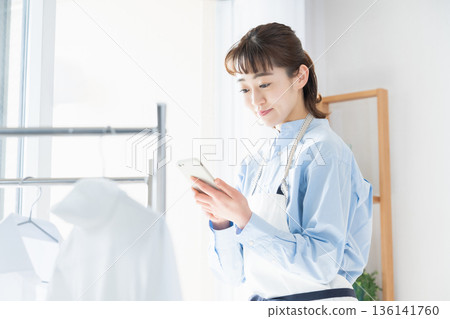 A young woman looking at her smartphone while doing housework A young woman looking at her smartphone while doing housework 136141760