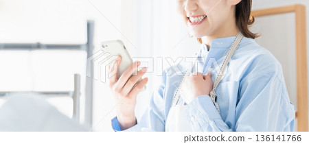 A young woman looking at her smartphone while doing housework 136141766