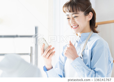A young woman looking at her smartphone while doing housework 136141767