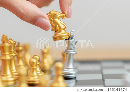 hand moving gold Chess knight figure and Checkmate opponent during chessboard competition. Strategy, Success, management, business planning, win, disruption, Trade war and leadership concept hand moving gold Chess knight figure and Checkmate opponent during chessboard competition. Strategy, Success, management, business planning, win, disruption, Trade war and leadership concept 136141874