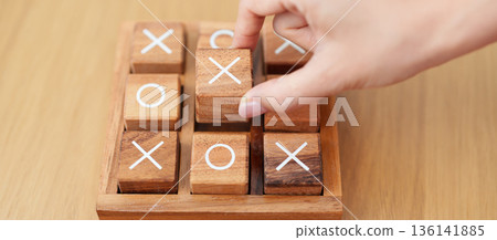 Hand holding and playing wooden block of tic tac toe game. A completed game of noughts and crosses or Xs and Os game. Challenge, Competition, winning, tactic, strategy and recreation concepts Hand holding and playing wooden block of tic tac toe game. A completed game of noughts and crosses or Xs and Os game. Challenge, Competition, winning, tactic, strategy and recreation concepts 136141885