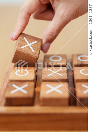 Hand holding and playing wooden block of tic tac toe game. A completed game of noughts and crosses or Xs and Os game. Challenge, Competition, winning, tactic, strategy and recreation concepts Hand holding and playing wooden block of tic tac toe game. A completed game of noughts and crosses or Xs and Os game. Challenge, Competition, winning, tactic, strategy and recreation concepts 136141887