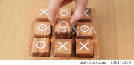 Hand holding and playing wooden block of tic tac toe game. A completed game of noughts and crosses or Xs and Os game. Challenge, Competition, winning, tactic, strategy and recreation concepts 136141890