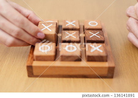 Hand holding and playing wooden block of tic tac toe game. A completed game of noughts and crosses or Xs and Os game. Challenge, Competition, winning, tactic, strategy and recreation concepts Hand holding and playing wooden block of tic tac toe game. A completed game of noughts and crosses or Xs and Os game. Challenge, Competition, winning, tactic, strategy and recreation concepts 136141891