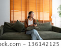 Happy young asian woman relax on comfortable couch at home texting messaging on smartphone 136142125