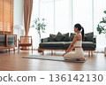 Asian woman sits on an exercise mat, getting ready to exercise in living room at home 136142130
