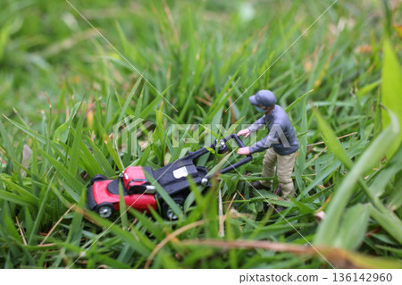 Miniature Worker Pushing Lawn Mower Through Green Grass Miniature Worker Pushing Lawn Mower Through Green Grass 136142960