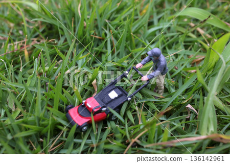 Miniature Worker Pushing Lawn Mower Through Green Grass Miniature Worker Pushing Lawn Mower Through Green Grass 136142961