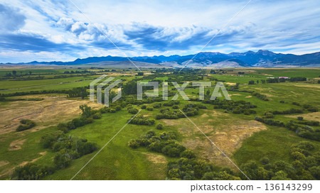 Aerial Lush Green Fields and Mountain Range Under Dramatic Sky Wyoming 136143299