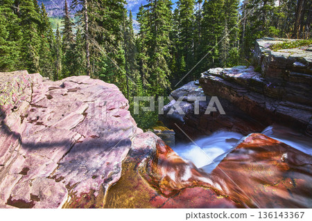 Waterfall and Red Rock Ledges with Evergreen Forest in Sunlight 136143367