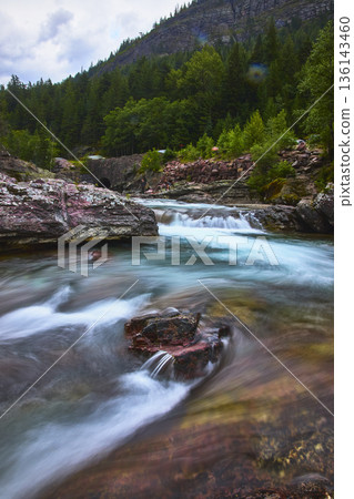 Red Rock River Cascades and Lush Forest in Mountain Landscape Glacier National Park Red Rock River Cascades and Lush Forest in Mountain Landscape Glacier National Park 136143460