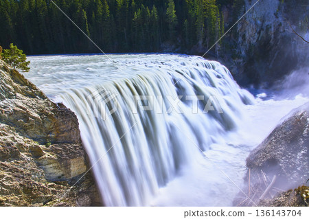 Powerful Waterfall Flowing Over Rocky Cliff With Lush Forest In Background Powerful Waterfall Flowing Over Rocky Cliff With Lush Forest In Background 136143704