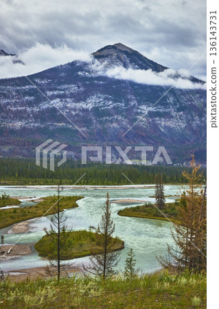 Snow Capped Mountain River and Evergreen Forest in Jasper Under Cloudy Sky 136143731
