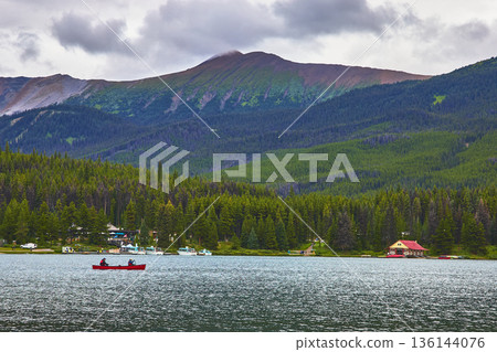 Canoe on Lake with Forest and Mountain Backdrop under Cloudy Sky Canoe on Lake with Forest and Mountain Backdrop under Cloudy Sky 136144076