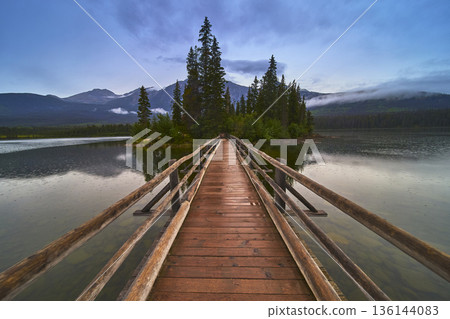 Bridge Leading to Forested Island on Calm Lake with Mountain Backdrop at Dusk Bridge Leading to Forested Island on Calm Lake with Mountain Backdrop at Dusk 136144083