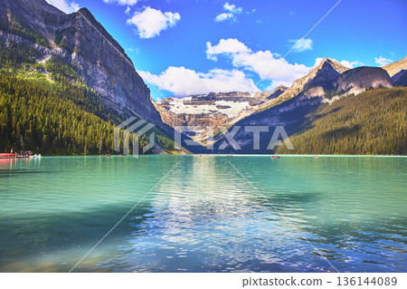 Turquoise Glacier Lake Surrounded by Mountains and Evergreen Forest in Bright Sunlight 136144089
