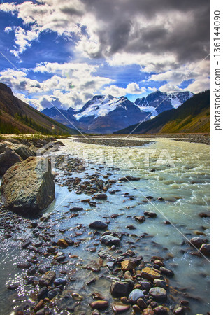 Glacial River Flowing Toward Snow Capped Peaks Under Cloudy Sky Mountain Landscape Glacial River Flowing Toward Snow Capped Peaks Under Cloudy Sky Mountain Landscape 136144090