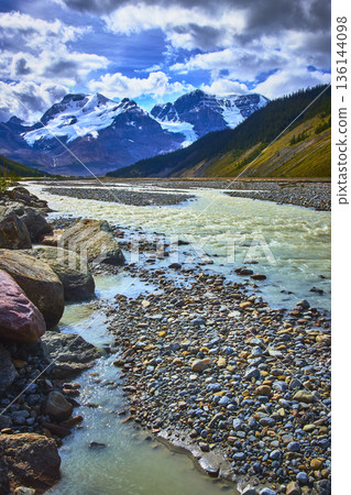 Athabasca Glacier Meltwater River Flowing Through Rocky Valley with Snowy Mountain Peaks 136144098