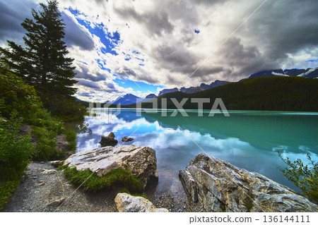 Turquoise Lake with Rocky Shore and Pine Trees against Mountain Backdrop Turquoise Lake with Rocky Shore and Pine Trees against Mountain Backdrop 136144111