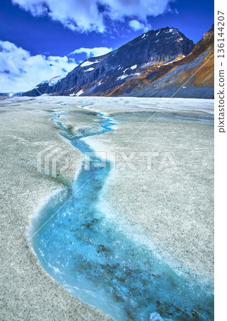 Athabasca Glacier Meltwater Stream and Rugged Mountain Under Blue Sky 136144207