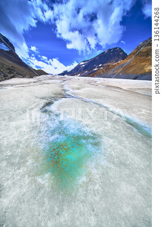 Athabasca Glacier Melting Ice Pool with Rocky Mountain Peaks and Dramatic Blue Sky 136144268