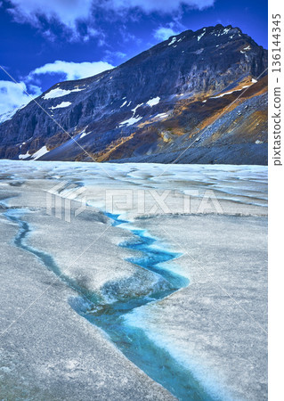 Athabasca Glacier Meltwater Stream and Rugged Mountain Under Blue Sky 136144345