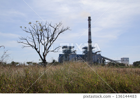 Power plant rising above dry grass under a cloudy sky with natural light, conveying energy production in an environmental context Power plant rising above dry grass under a cloudy sky with natural light, conveying energy production in an environmental context 136144483