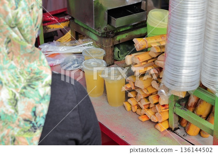 Indonesian Sugar Cane Juice Vendor Preparing Refreshments with Natural Light for Local Street Food Experience Indonesian Sugar Cane Juice Vendor Preparing Refreshments with Natural Light for Local Street Food Experience 136144502