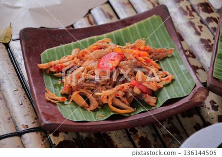 Indonesian Spicy Squid Dish Served on Banana Leaf, showcasing the vibrant colors and textures of traditional Southeast Asian cuisine under natural light 136144505