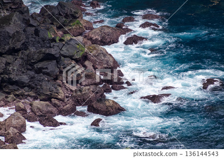 Turbulent ocean waves crashing over dark rugged volcanic rock formations at the coastline. Turbulent ocean waves crashing over dark rugged volcanic rock formations at the coastline. 136144543