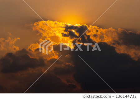Golden sun behind dark clouds with warm light in the sky Golden sun behind dark clouds with warm light in the sky 136144732