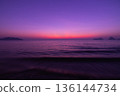Purple sunset sky over calm sea with soft waves and distant islands, peaceful evening light and quiet ocean mood 136144734