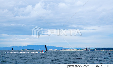 在陰雲密佈的天空下，相模灣裡許多遊艇悠閒航行，一艘藍色快艇飛馳在海面上。 136145640