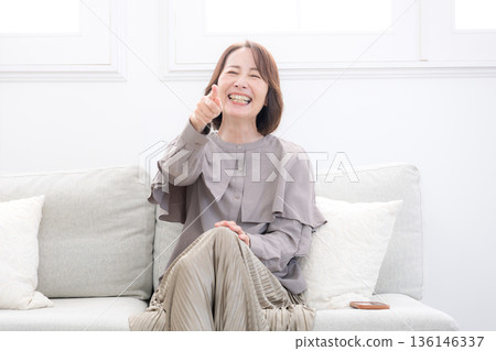 Smiling senior woman laughing out loud while watching TV in the living room 136146337