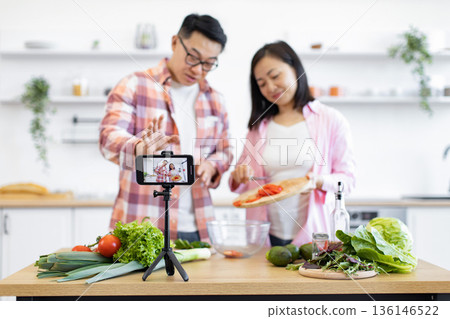 A couple films a cooking tutorial in their bright, modern kitchen, preparing fresh ingredients for a healthy meal A couple films a cooking tutorial in their bright, modern kitchen, preparing fresh ingredients for a healthy meal 136146522