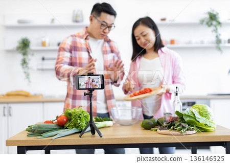 A couple films a cooking tutorial in their kitchen, preparing fresh ingredients for a delicious meal A couple films a cooking tutorial in their kitchen, preparing fresh ingredients for a delicious meal 136146525