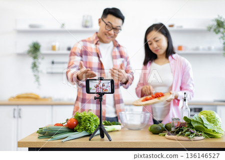 An Asian couple is preparing a meal in their kitchen while recording a video for their online audience 136146527