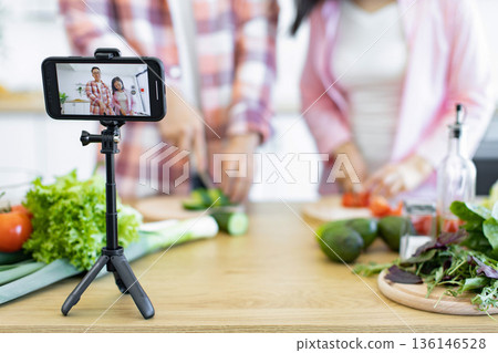 A family is recording a cooking video in the kitchen, preparing fresh vegetables for a healthy meal A family is recording a cooking video in the kitchen, preparing fresh vegetables for a healthy meal 136146528
