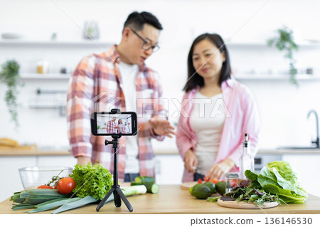 An Asian couple films a cooking vlog in their kitchen, preparing fresh vegetables for a healthy meal 136146530