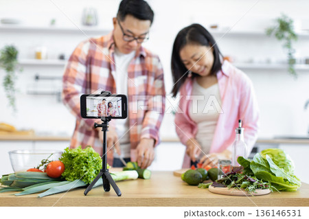 A couple is recording a cooking video in their kitchen, preparing fresh ingredients for a delicious meal A couple is recording a cooking video in their kitchen, preparing fresh ingredients for a delicious meal 136146531