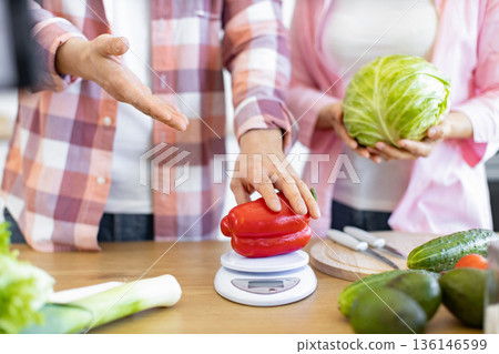 Two people are preparing fresh vegetables for a healthy meal, including a red bell pepper and cabbage 136146599