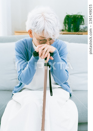 Depressed senior woman with a cane in her hand in the living room Depressed senior woman with a cane in her hand in the living room 136149055