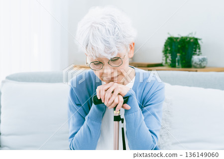 Depressed senior woman with a cane in her hand in the living room 136149060