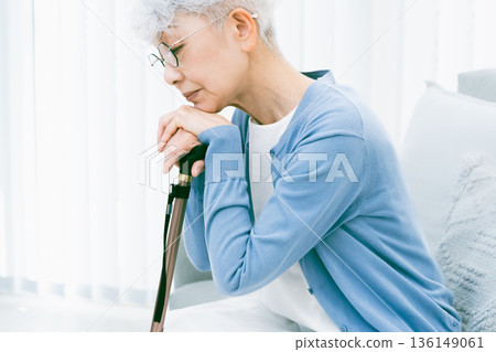 Depressed senior woman with a cane in her hand in the living room 136149061