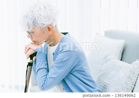 Depressed senior woman with a cane in her hand in the living room Depressed senior woman with a cane in her hand in the living room 136149062