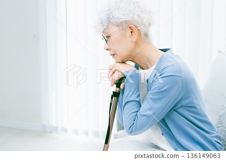 一位情緒低落的老婦人拄著拐杖坐在客廳裡 一位情緒低落的老婦人拄著拐杖坐在客廳裡 136149063