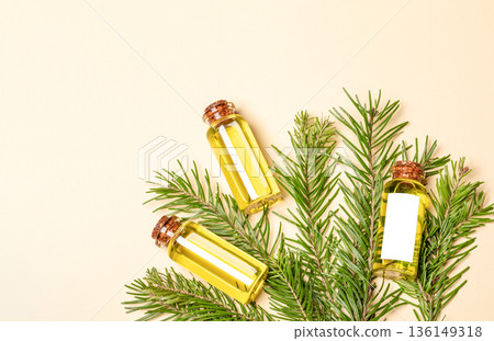 Three essential fir oil bottles with pikhta branches on beige background. Copt space top view Three essential fir oil bottles with pikhta branches on beige background. Copt space top view 136149318